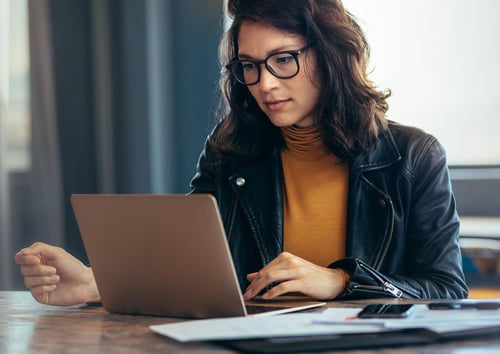 female with dark hair looking at laptop wearing black jacket and yellow shirt